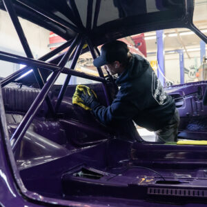 Aden Baker detailing a purple Porche inside an auto body shop during a full polishing.