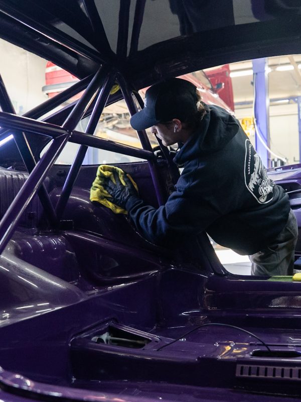 Aden Baker detailing a purple Porche inside an auto body shop during a full polishing.